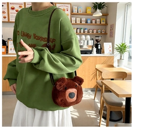 Detail of plush brown bear tote bag with soft ears shown on a green sweatshirt