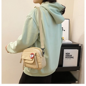 Detail of beige canvas crossbody bag featuring a cartoon badge and adjustable wide strap