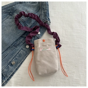 Detail view of corduroy crossbody bag with purple pleated strap and orange button accent