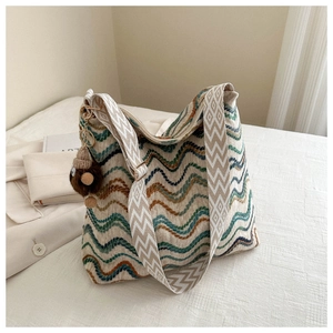 Detail of woven tote bag with colorful wave patterns and a decorative plush acorn charm