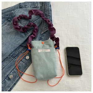 Detail of mint green corduroy mini crossbody bag with purple pleated strap and orange drawstring