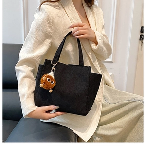 Detailed view of black corduroy tote bag with cute brown plush charm on handles