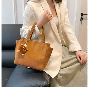 Brown corduroy handbag with plush charm shown in a cozy indoor lifestyle setting