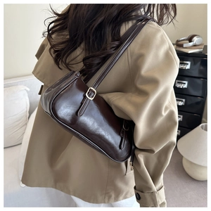 Detail of deep brown glossy baguette bag with gold buckle on a shoulder strap