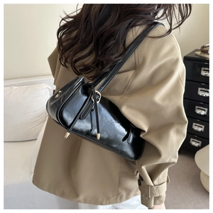 Detail of a black glossy baguette bag with gold buckles worn over a beige trench coat