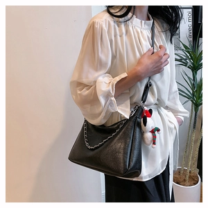 Detail view of black pleated tote bag with silver chain and cute plush bear charm