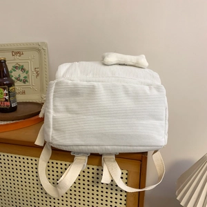 White corduroy backpack with bone charm for students shown on a wooden cabinet