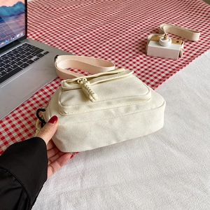 Chic cream canvas crossbody bag with flap pocket and decorative woven zipper pull