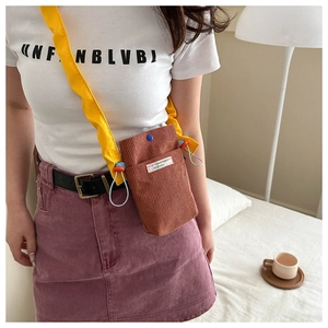 Close-up of brown corduroy mini crossbody bag with yellow strap on a person