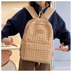 Detail view of khaki plaid backpack showing leather logo patch and front zipper pocket