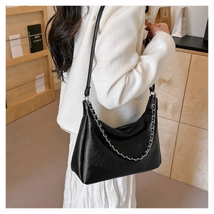Detail of black pleated tote bag with shiny leather texture and silver chain strap