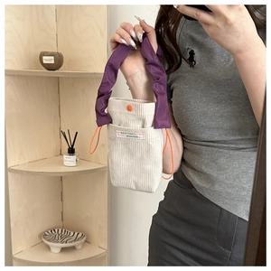 Detail of corduroy drawstring bucket bag with purple pleated handle and logo patch
