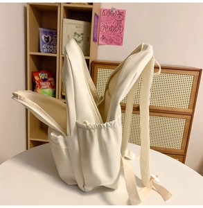 Close-up of cream white minimalist backpack with multiple pockets on a wooden desk