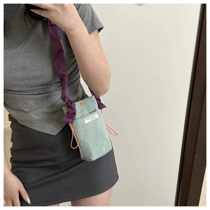 Detail of mint green corduroy phone bag with purple pleated strap and orange drawstring