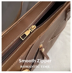 Detail of dark brown leather tote featuring white contrast stitching and gold metal zipper
