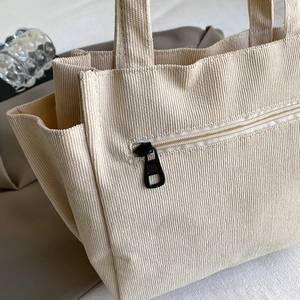 Minimalist cream corduroy tote bag with textured stripes and front zipper detail