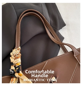 Detail of a brown leather tote handle with a stylish silk scarf wrap and white stitching