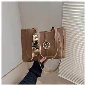 Gros plan du sac cabas marron avec surpiqûres blanches et logo M doré sur le devant