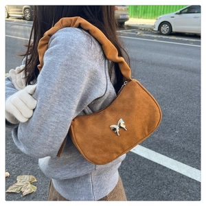 Close-up of brown suede underarm bag featuring silver butterfly charm and ruched handle