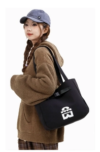 Detail of black canvas tote bag with geometric logo carried by model in fleece hoodie