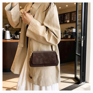 Detail of cross-stitched dark brown suede bag with gold chain strap in a cafe setting