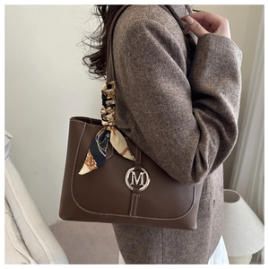 Détail du grand sac cabas marron avec logo M en métal et foulard en soie sur l'anse