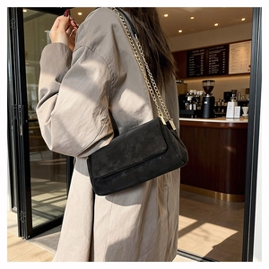 Detail of black suede messenger bag with gold chain strap in a cafe setting