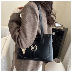 Détail du sac fourre-tout en cuir noir avec coutures blanches et logo métallique doré en M