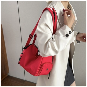 Detail view of red nylon crossbody bag with adjustable strap worn by model in beige trench coat