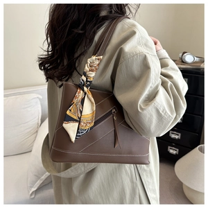 Detail of a brown tote bag with contrast stitching and a vintage patterned silk scarf handle