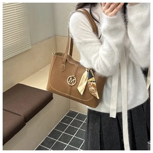 Détail d'un grand sac cabas marron avec logo M doré et foulard floral sur l'anse