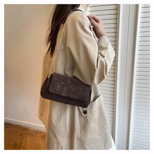 Detail of dark brown matte leather messenger bag with golden chain strap on shoulder
