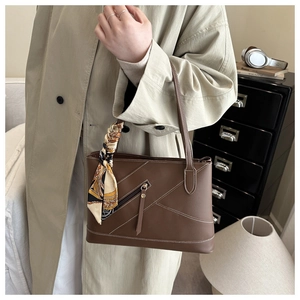 Detail van bruine lederen tote bag met stiksels en decoratieve zijden sjaal