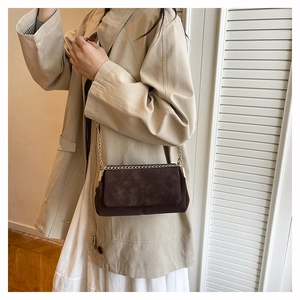 Detailed view of deep brown suede crossbody bag with gold chain strap on a model