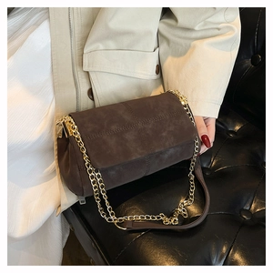 Detail of dark brown suede crossbody bag with gold chain and cross-stitch texture