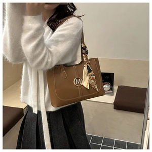 Détail d'un sac cabas marron en cuir brillant avec breloque M dorée et foulard en soie