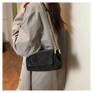 Detail of black crossbody bag with gold chain strap and cross stitching on soft texture