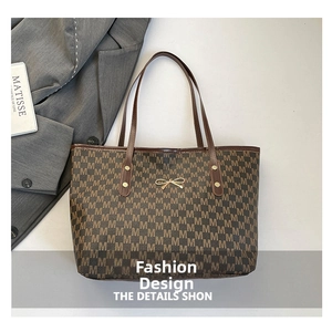 Detail of golden bow charm on brown monogrammed tote bag for women's daily commuting