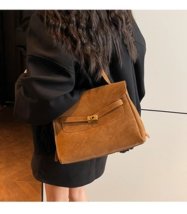 Borsa a mano in pelle marrone con chiusura a scatto indossata da modella in blazer nero