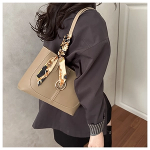 Détail d'un sac cabas en cuir kaki avec foulard décoratif et logo métallique circulaire