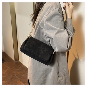 Detail of black suede shoulder bag featuring gold chain strap and crisscross stitching