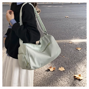 Pale green large gym bag with adjustable strap worn by a model on an autumn street