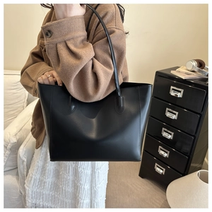 Vue détaillée d'un grand sac cabas en cuir noir porté à l'épaule dans un décor d'intérieur