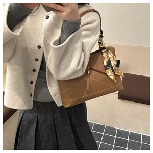 Close-up of brown leather tote with geometric stitching and silk scarf on handle