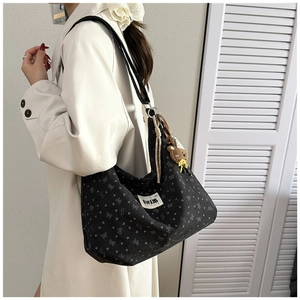 Detail of black floral canvas hobo bag with bow patterns and cute teddy bear charm