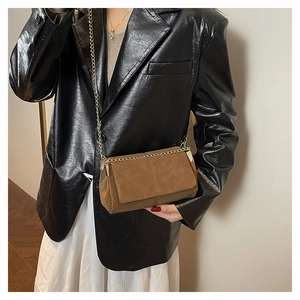 Detailed view of brown matte crossbody bag featuring cross-stitch and gold chain strap