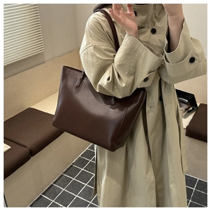 Grand sac cabas en cuir marron porté par un mannequin en trench-coat moderne