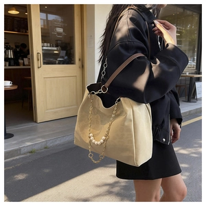 Detail of beige tote bag featuring elegant gold chain with white pearl accents and leather strap