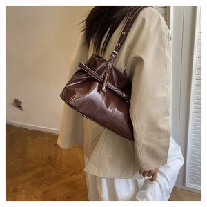Detail of dark brown patent leather shoulder bag with adjustable silver buckle strap