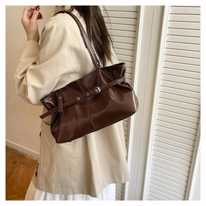 Detail of dark brown patent leather tote bag with metal buckle on a shoulder strap